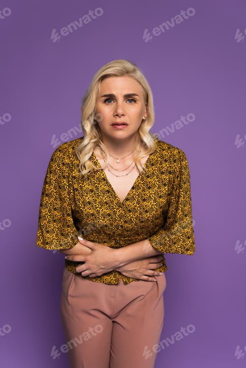 Preview: blonde woman with stomach ache touching belly during climax isolated on purple