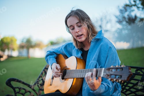 Preview: Teenager singing and playing the guitar on a bench