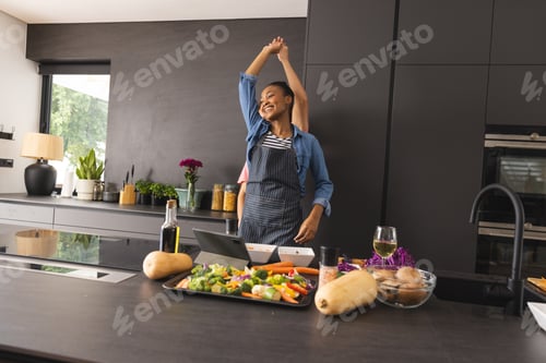 Preview: Happy diverse couple in aprons preparing meal having fun dancing in kitchen