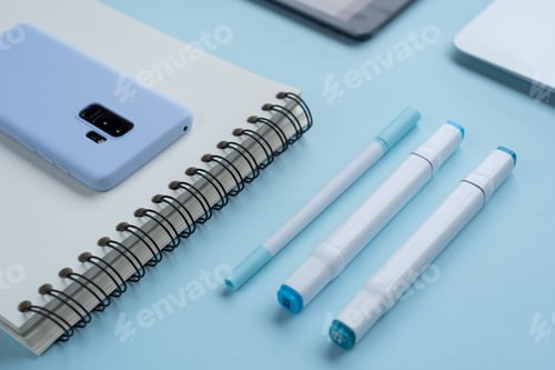 Preview: Close up shot of markers, pens, a notebook and a phone on a blue desk