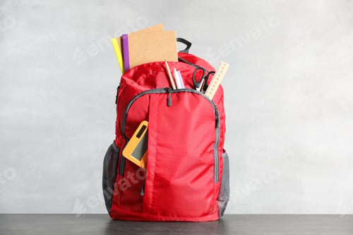Preview: Red backpack with stationery on grey table against light background