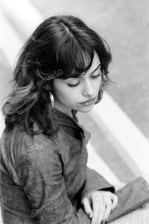 Preview: Elevated monochrome portrait of young woman sitting on the street.