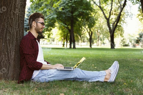 Man sitting on grass with laptop outdoors