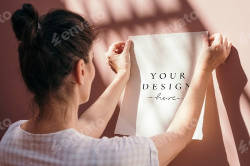 Preview: Woman attaching a white poster mockup to a pastel pink wall