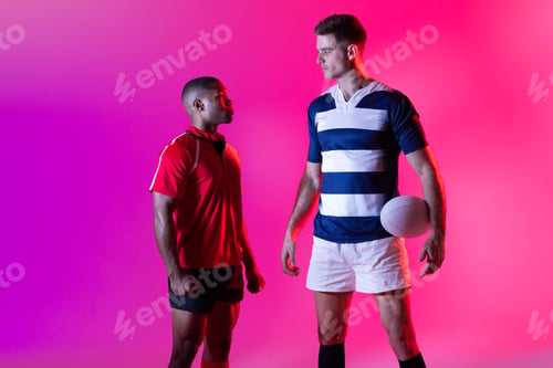 Preview: Diverse male rugby players with rugby ball over pink lighting