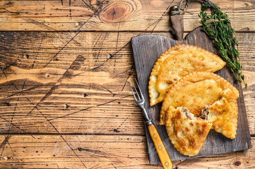 Preview: Chilean fried empanadas filled with minced beef meat served on a wooden cutting board.