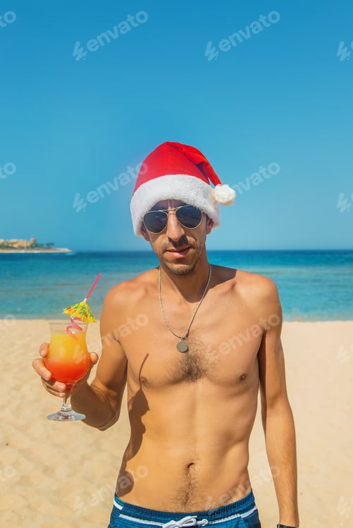 Preview: man in a santa hat is resting on the sea. Drinks a cocktail. Selective focus.