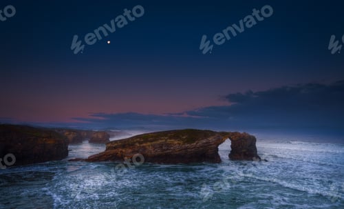 Preview: Full moon at sunrise over the rocky arch of As Catedrais