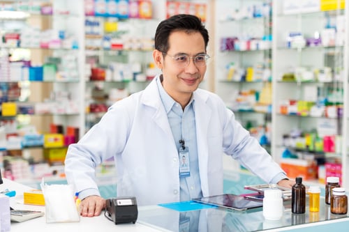 Preview: Smiling asian pharmacist man at counter at drugstore