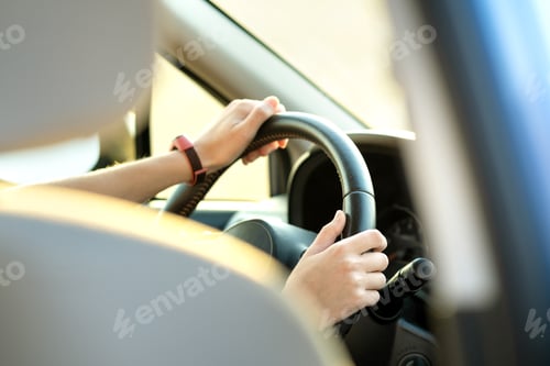 Preview: Close up view of woman hands holding steering wheel driving a car on city street on sunny day.