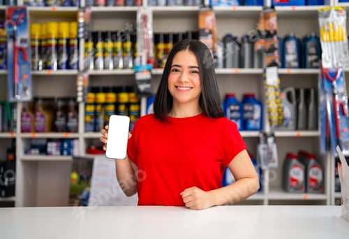 Preview: Young woman working in an auto parts store holding a smartphone with a blank white screen