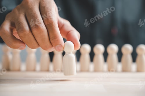 Preview: Hand holding a white wooden figure above a row of figures on a wood table.