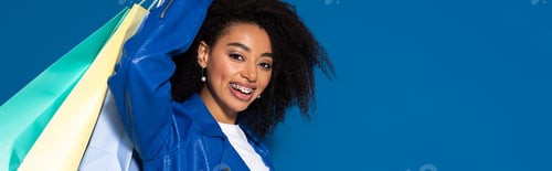Preview: smiling african american woman with shopping bags isolated on blue background, panoramic shot