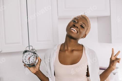 Preview: cheerful african american woman holding clock and showing peace sign