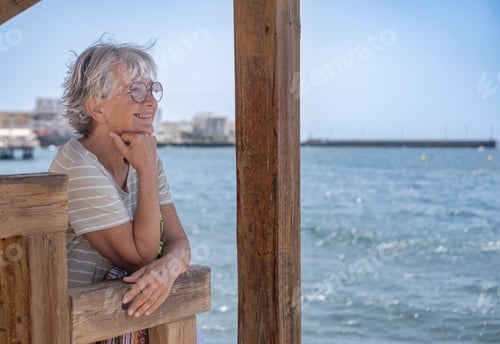 Preview: Portrait of cheerful senior woman sitting in the shade of the gazebo face the sea while looking away