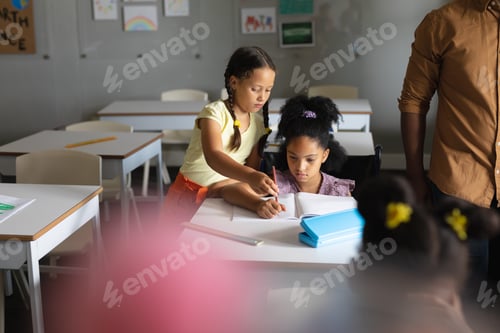 Visualização: Estudante do ensino fundamental caucasiano auxiliando colega biracial estudando na mesa em sala de aula