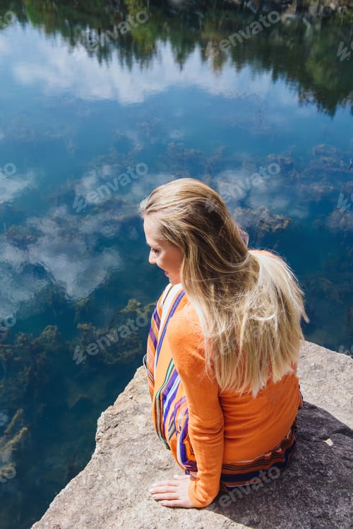 Preview: Beautiful blonde woman enjoying blue lake water on the high cliff in summer. Concept of freedom outd