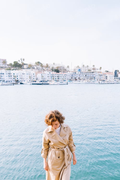 Preview: A thoughtful beautiful girl in a classic trench coat stands against the background of the sea