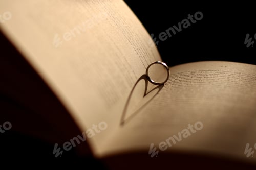 Preview: Ring inside of an open book with a shadow resembling a heart - concept of love