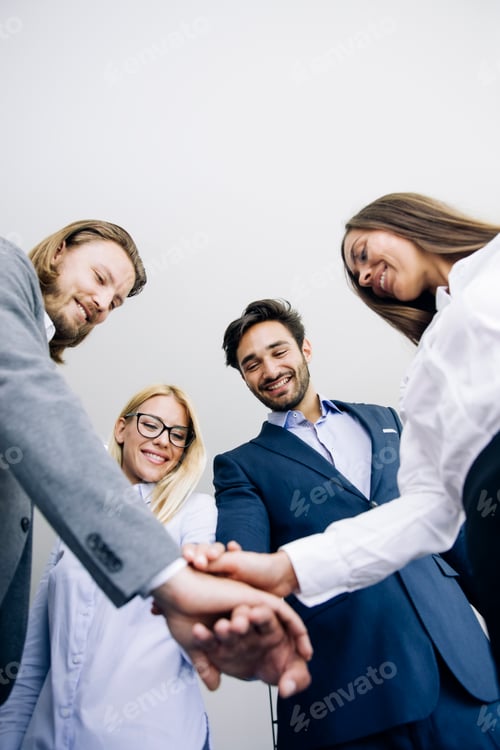 Preview: Young coworkers putting hands together as symbol of unity in the office