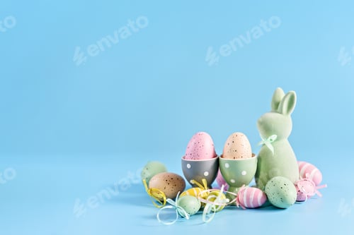 Preview: Pastel Easter Bunny Figurine Surrounded by Decorative Eggs on a Blue Background