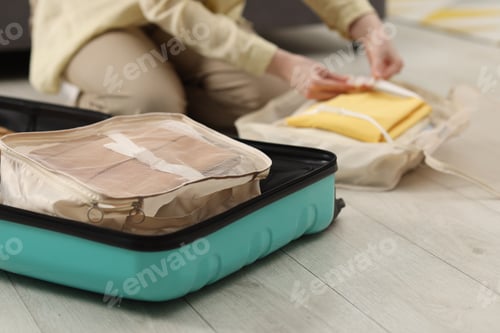 Preview: Woman packing her belongings into suitcase on floor indoors, selective focus