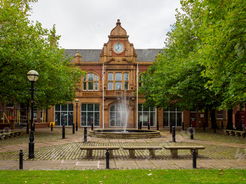 Preview: Fire Station Salford. Historic brick building with a clock tower, water fountain.