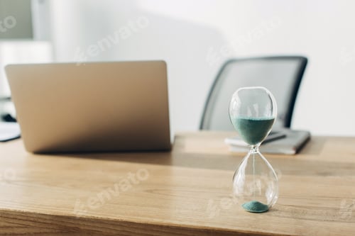 Preview: Selective focus of hourglass on table near laptop in office