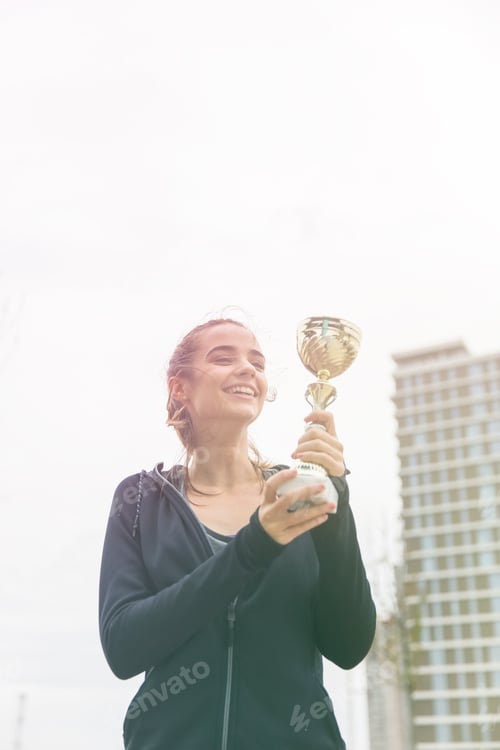 Preview: Happy sporty young woman holding gold trophy cup