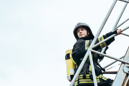 Preview: female firefighter in protective uniform and helmet with fire extinguisher on back standing on
