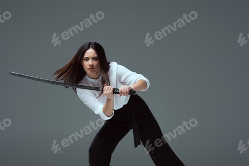 Preview: young asian woman fighting with katana sword isolated on grey