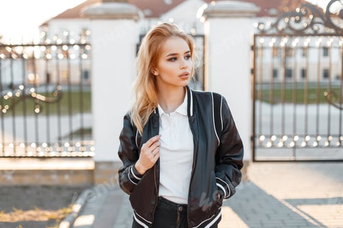 Preview: Pretty beautiful young blond woman in a black spring stylish jacket in white polo. American fashion