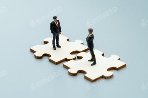 Preview: Miniature business figures stand on interlocking puzzle pieces.
