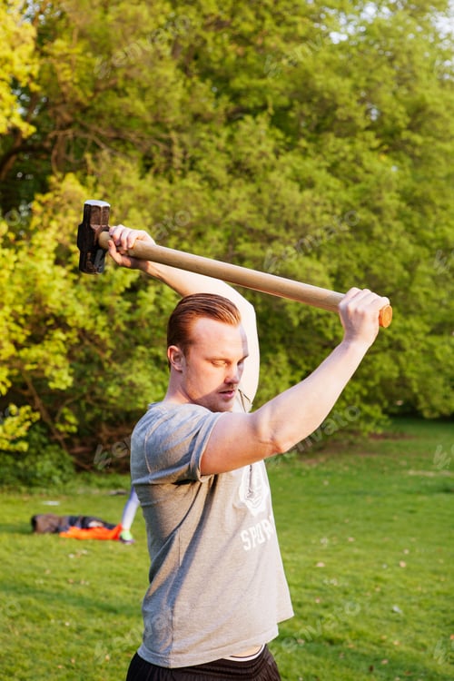 Preview: Young man lifting hammer in park