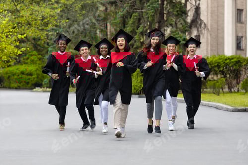 Preview: Cheerful multiracial students in graduation costumes walking by university campus