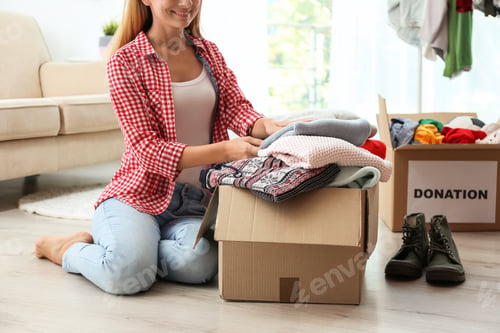 Preview: Woman packing clothes into donation box in living room