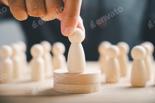 Preview: Hand placing wooden figure on a platform, surrounded by other figures. Leadership, team concept.