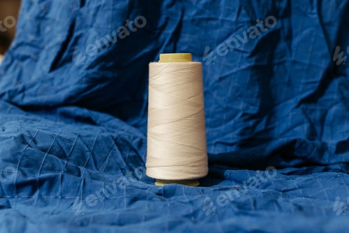 Preview: White spool of thread arranged neatly on a flat surface, with blue background
