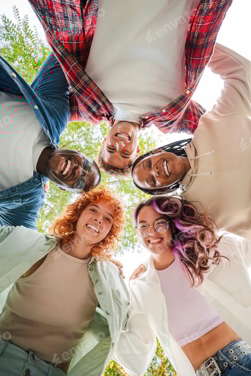Preview: Vertical. Low angle view of a group of multiracial happy young teenagers hugging each others in a