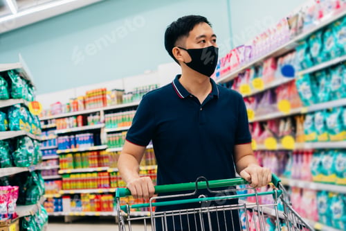 Preview: Asian man wearing a protective mask while shopping with cart trolley i supermarket store