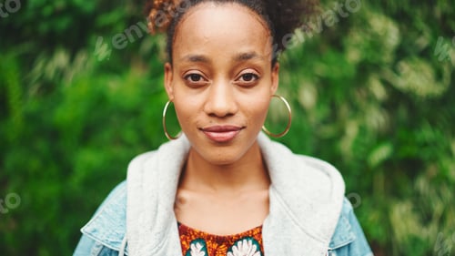 Preview: Closeup portrait African girl looking at camera and smiling in city park on green trees background