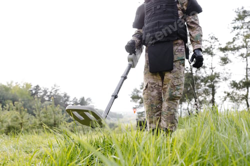 Preview: A man in a military uniform and bulletproof vest works in the forest with a metal detector