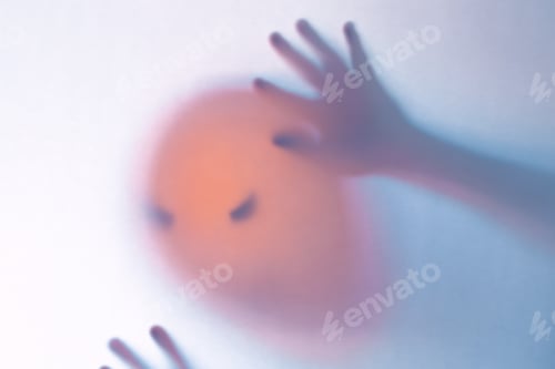 Preview: Halloween blurred background. A ghost resembling a pumpkin in color behind glass