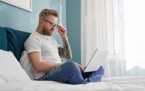 Preview: Male freelancer using laptop on bed