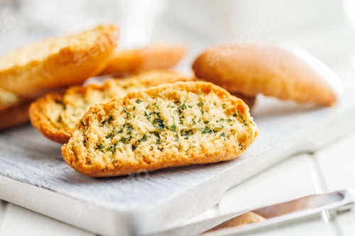 Preview: Garlic crisp bread Slices Topped With Herbs on cutting board.