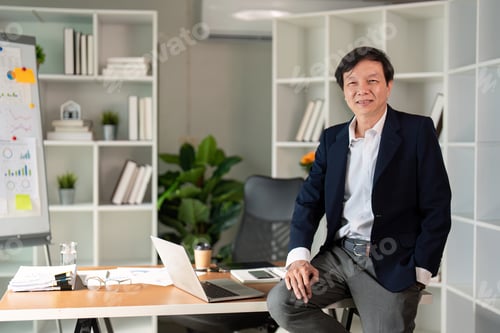Preview: Elderly businessman confidently seated at desk in modern office environment.