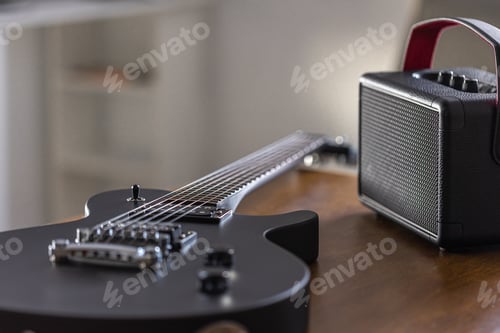 Preview: Black electric guitar and speaker on a wooden table.