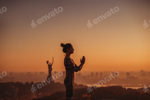 Preview: Woman doing yoga on the roof of a skyscraper in big city