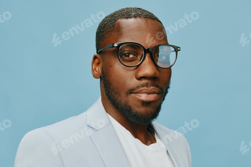 Preview: Portrait of a man with glasses, wearing a light jacket against a blue background, showcasing
