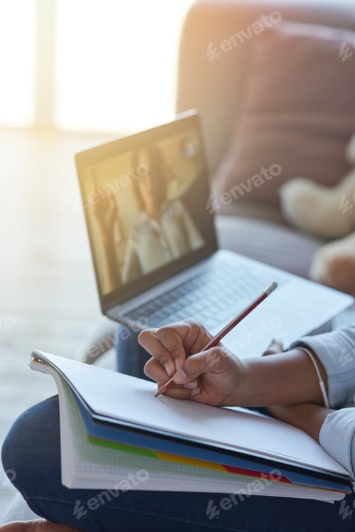 Preview: Close up shot of hands of teen schoolgirl making notes while having online lesson with teacher via
